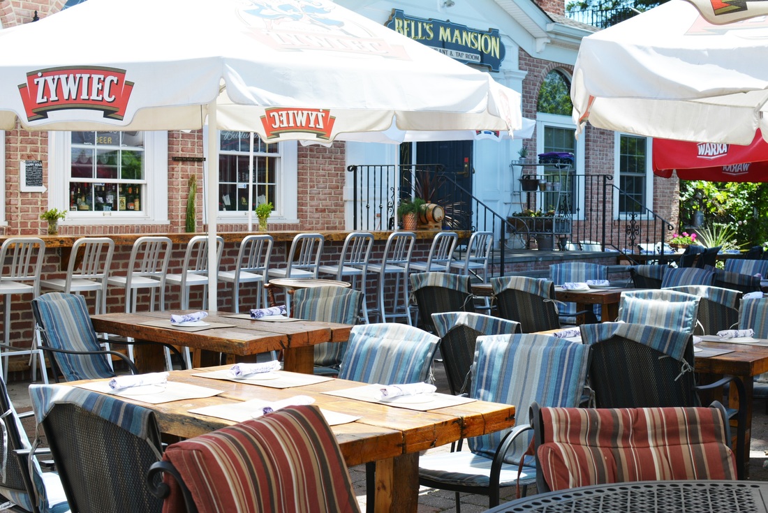Outdoor patio dining area with striped chairs, wooden tables, umbrellas, and Zywiec beer signage on brick building