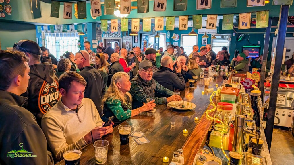 A crowded bar inside O’Reilly’s Pub & Grill in Newton, New Jersey, filled with patrons celebrating Saint Patrick’s Day beneath green Guinness decorations.