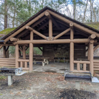 Log picnic pavilion with a stone fireplace, picnic tables, and barbecue grills at the Kittle Field day use area in Stokes State Forest.