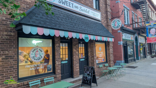 Sweet and Swirled storefront on a brick street in Newton with turquoise scalloped awning and matching outdoor seating.